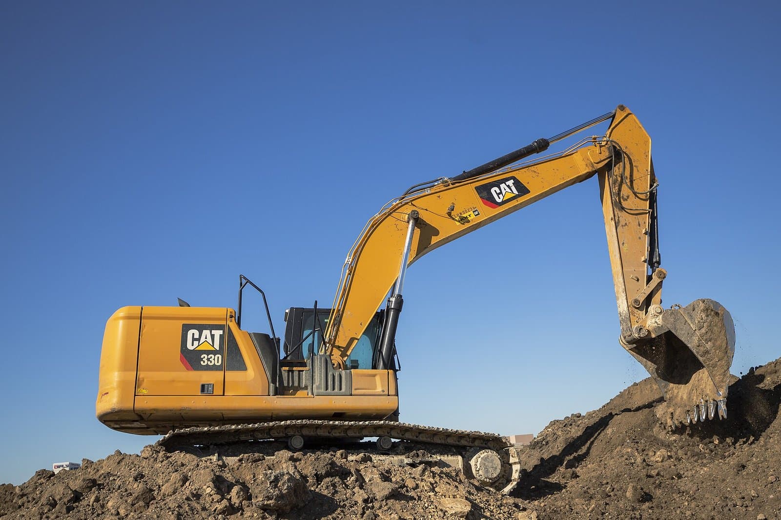Caterpillar 330 hydraulic excavator digging on a dirt pile against a blue sky